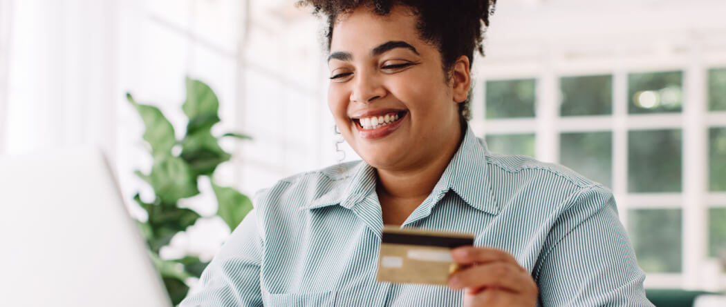 Woman in a bright kitchen holding a debit card and using a laptop