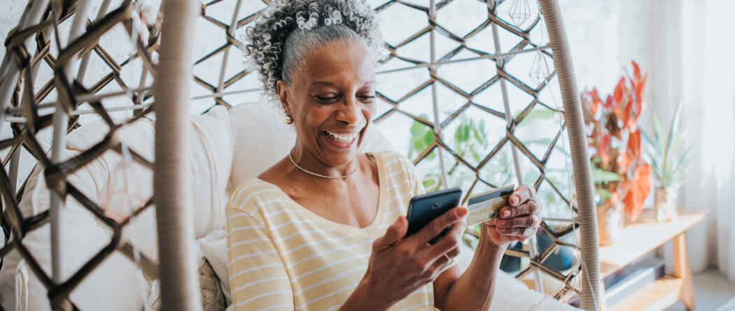 Older woman smiling and holding a smartphone and credit card
